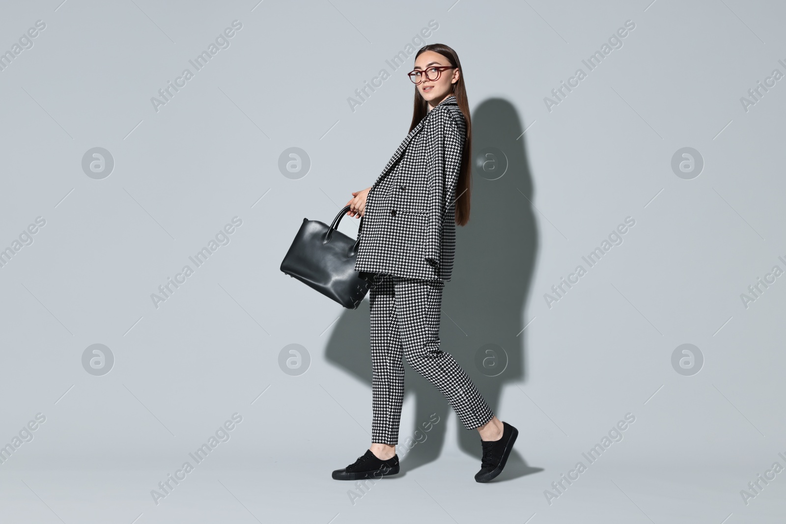 Photo of Beautiful woman in stylish suit and glasses with bag on gray background