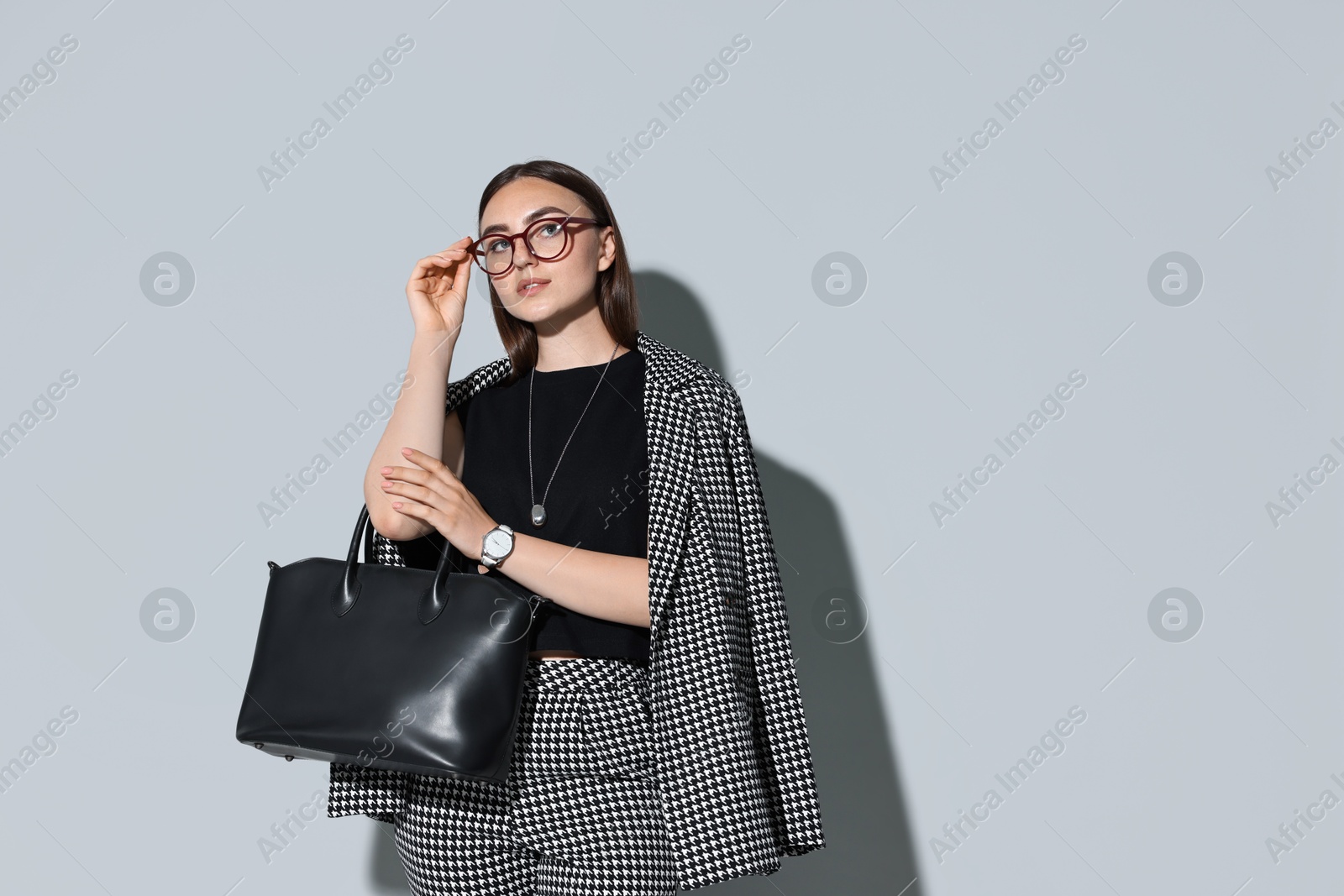 Photo of Beautiful woman in stylish suit and glasses with bag on gray background, space for text