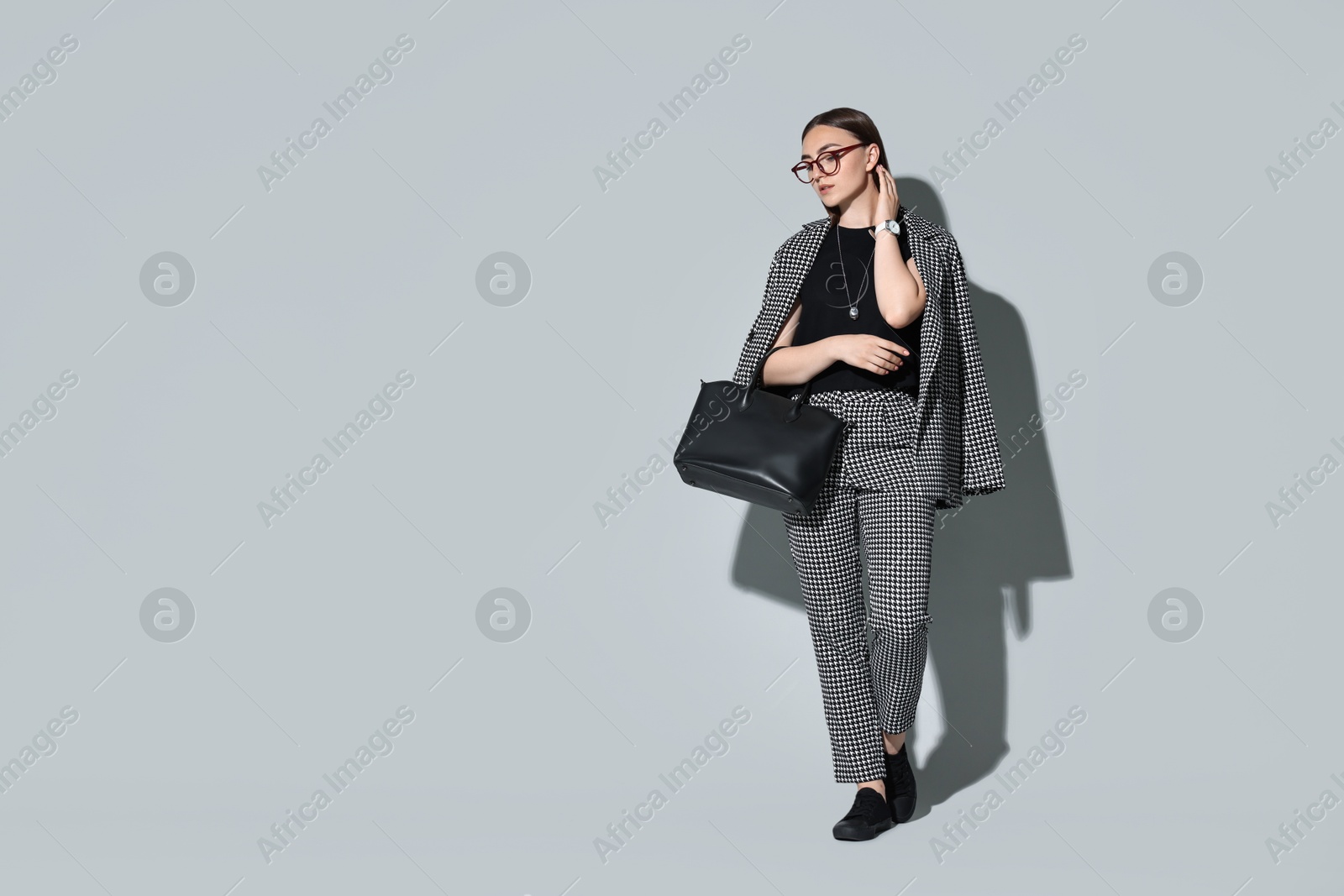 Photo of Beautiful woman in stylish suit and glasses with bag on gray background