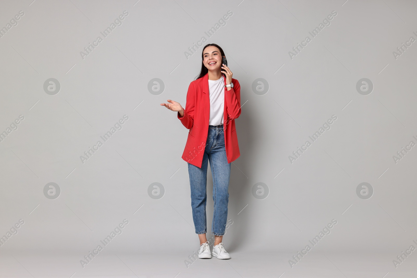 Photo of Beautiful woman in red jacket talking on phone against gray background