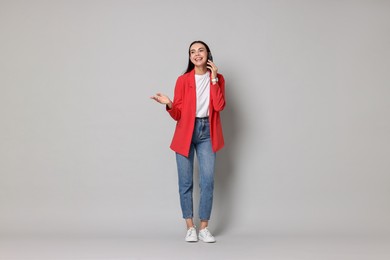 Photo of Beautiful woman in red jacket talking on phone against gray background