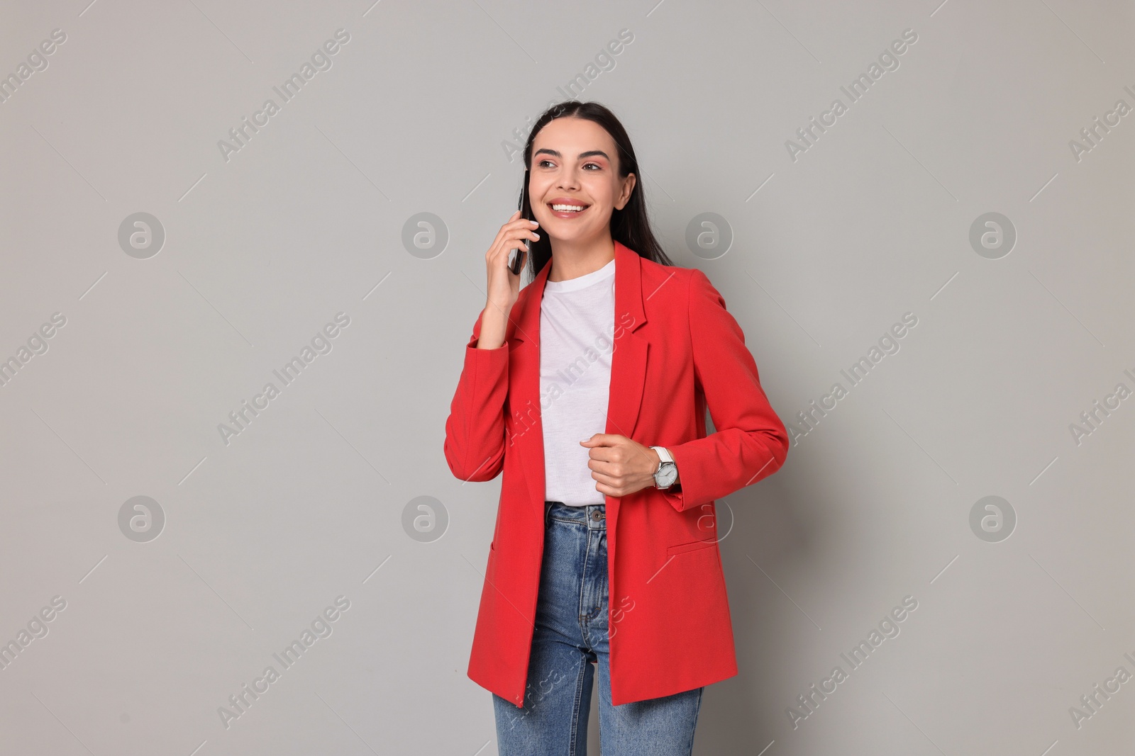 Photo of Beautiful woman in red jacket talking on phone against gray background