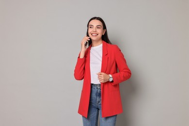 Photo of Beautiful woman in red jacket talking on phone against gray background