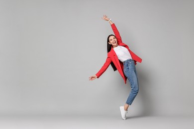 Photo of Cheerful woman in red jacket and jeans on gray background, space for text