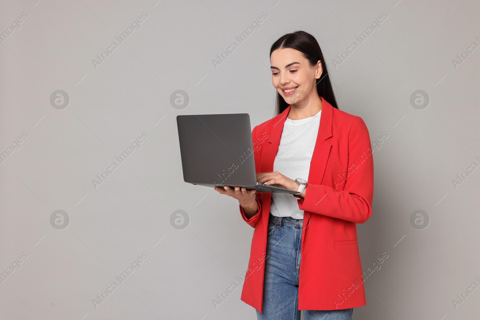 Photo of Beautiful woman in red jacket using laptop on gray background, space for text