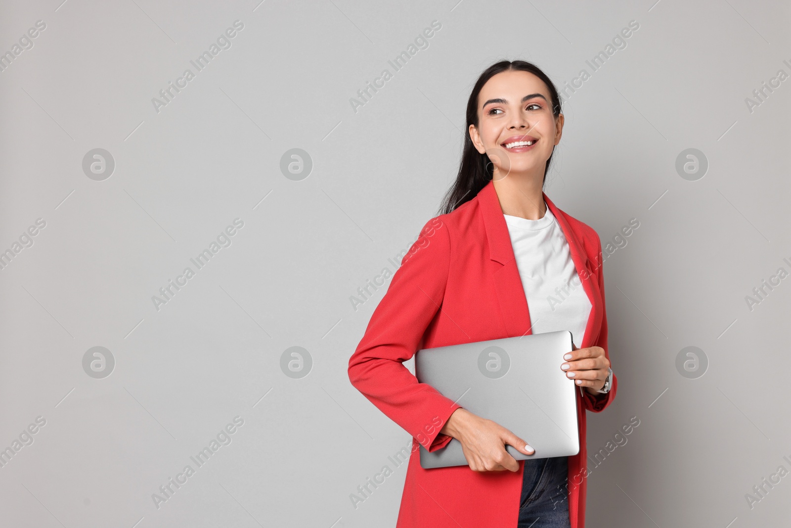 Photo of Beautiful woman in red jacket with laptop on gray background, space for text