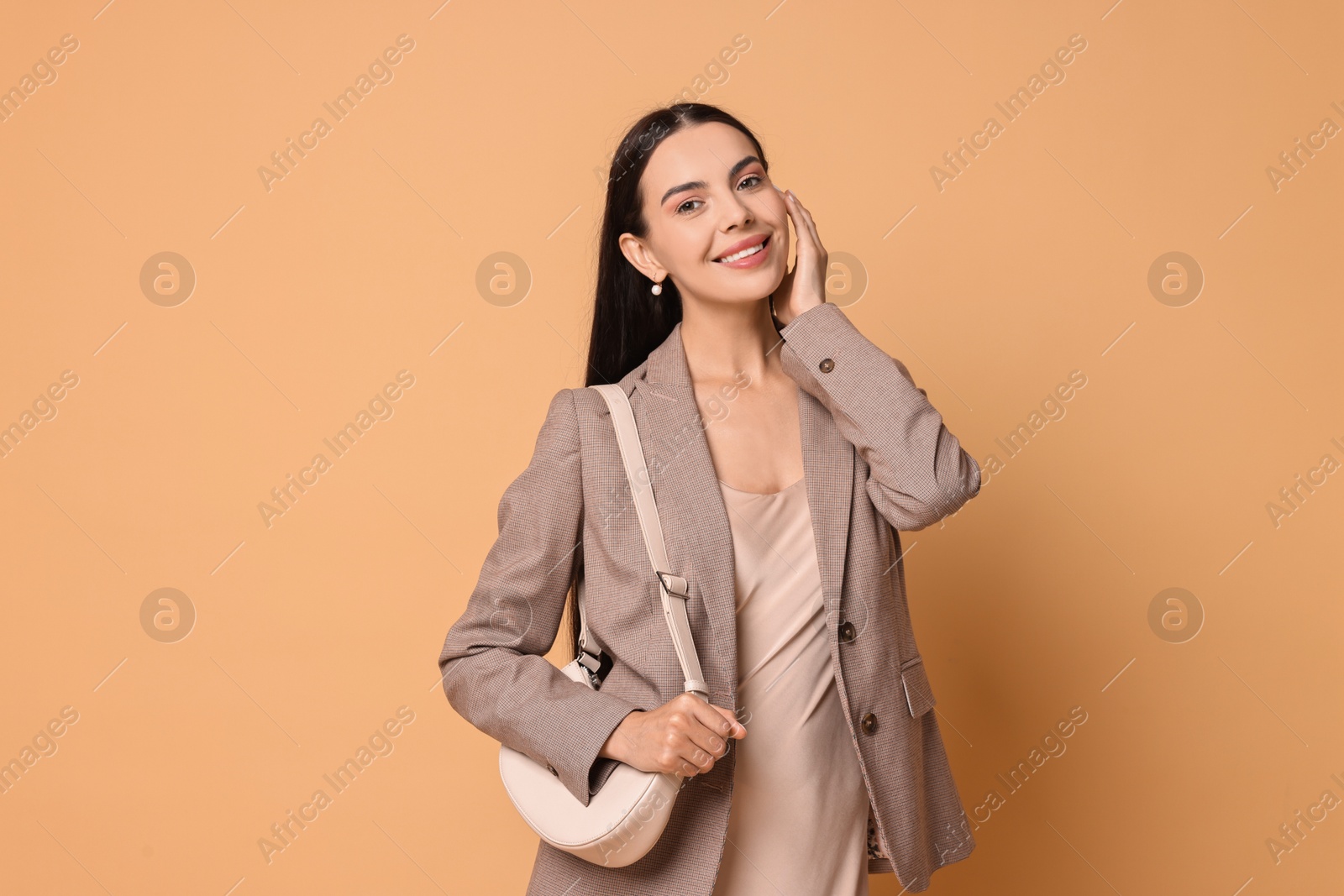 Photo of Beautiful woman in stylish jacket with bag on pale orange background