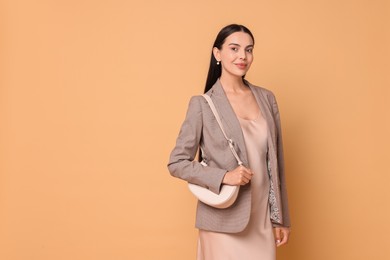 Photo of Beautiful woman in stylish jacket with bag on pale orange background, space for text