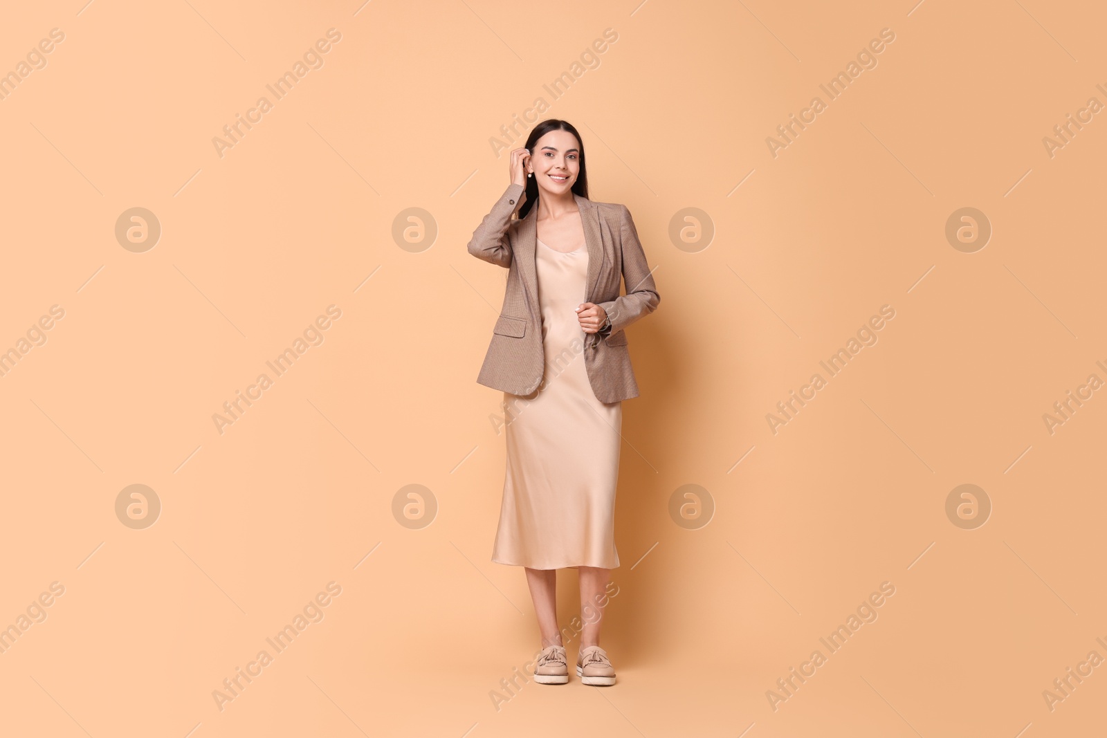 Photo of Beautiful woman in stylish jacket and beige dress on pale orange background