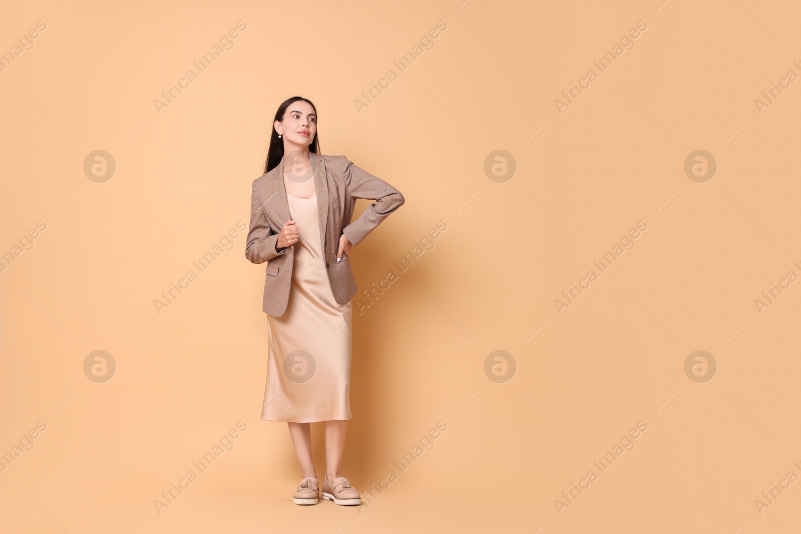 Photo of Beautiful woman in stylish jacket and beige dress on pale orange background, space for text