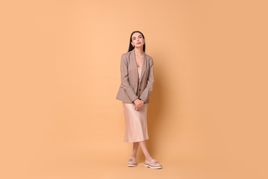 Photo of Beautiful woman in stylish jacket and beige dress on pale orange background