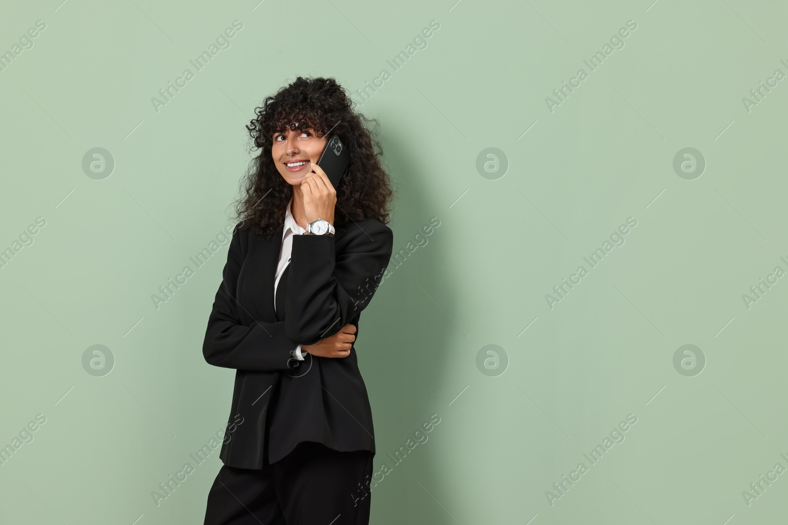 Photo of Beautiful young woman in stylish suit talking on smartphone against light olive background, space for text