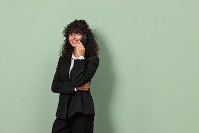 Photo of Beautiful young woman in stylish suit talking on smartphone against light olive background, space for text