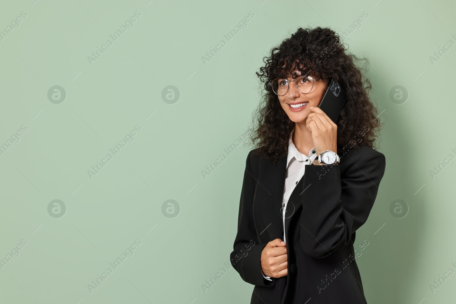 Photo of Beautiful young woman in stylish suit talking on smartphone against light olive background, space for text