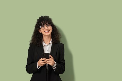 Beautiful young woman in stylish suit using smartphone on light olive background, space for text