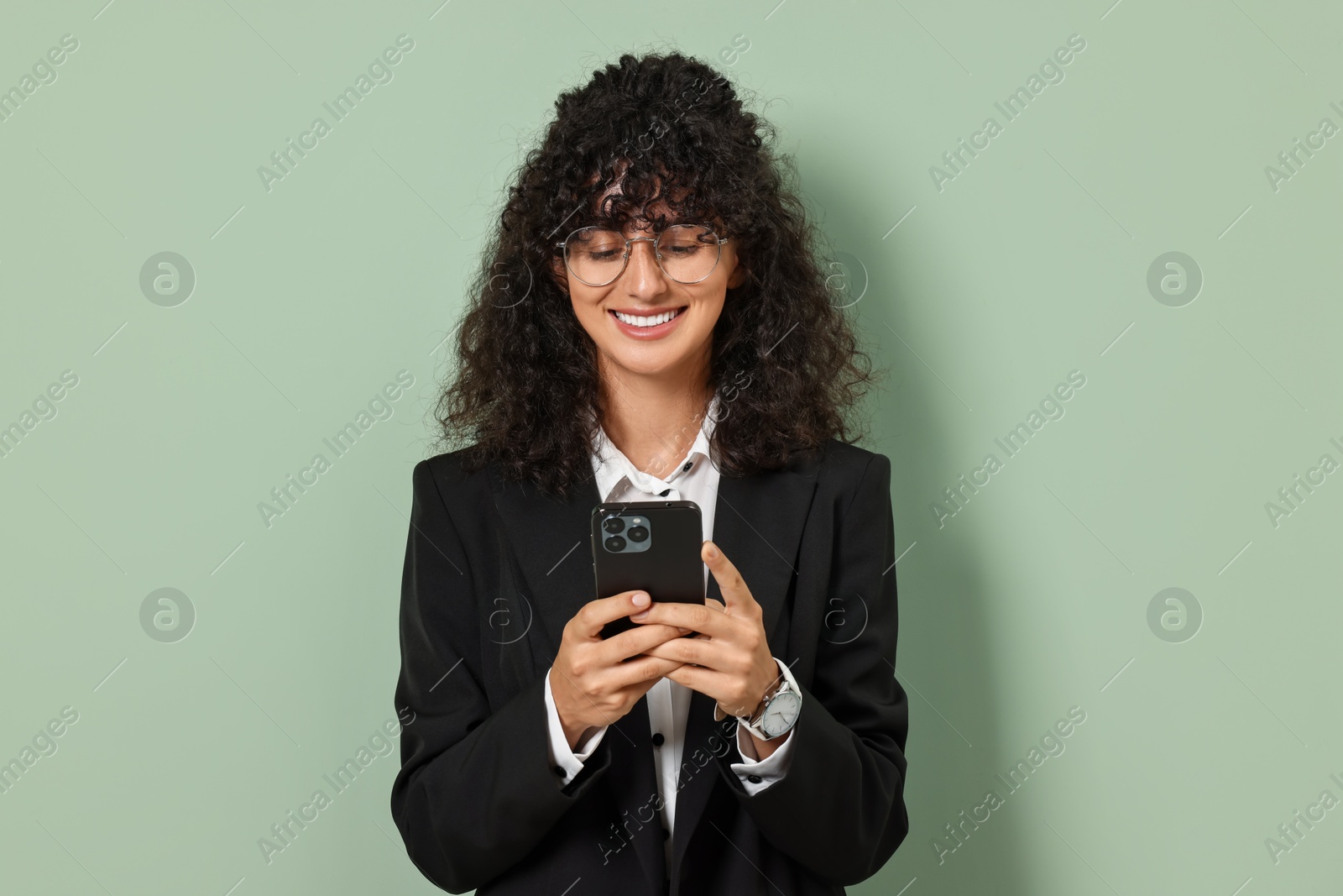 Photo of Beautiful young woman in stylish suit using smartphone on light olive background