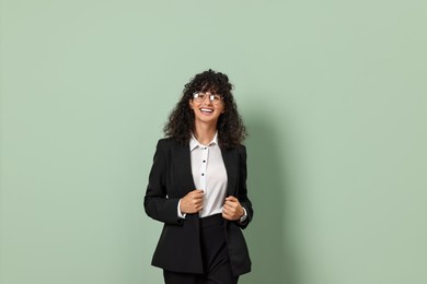 Beautiful young woman in stylish black suit on light olive background