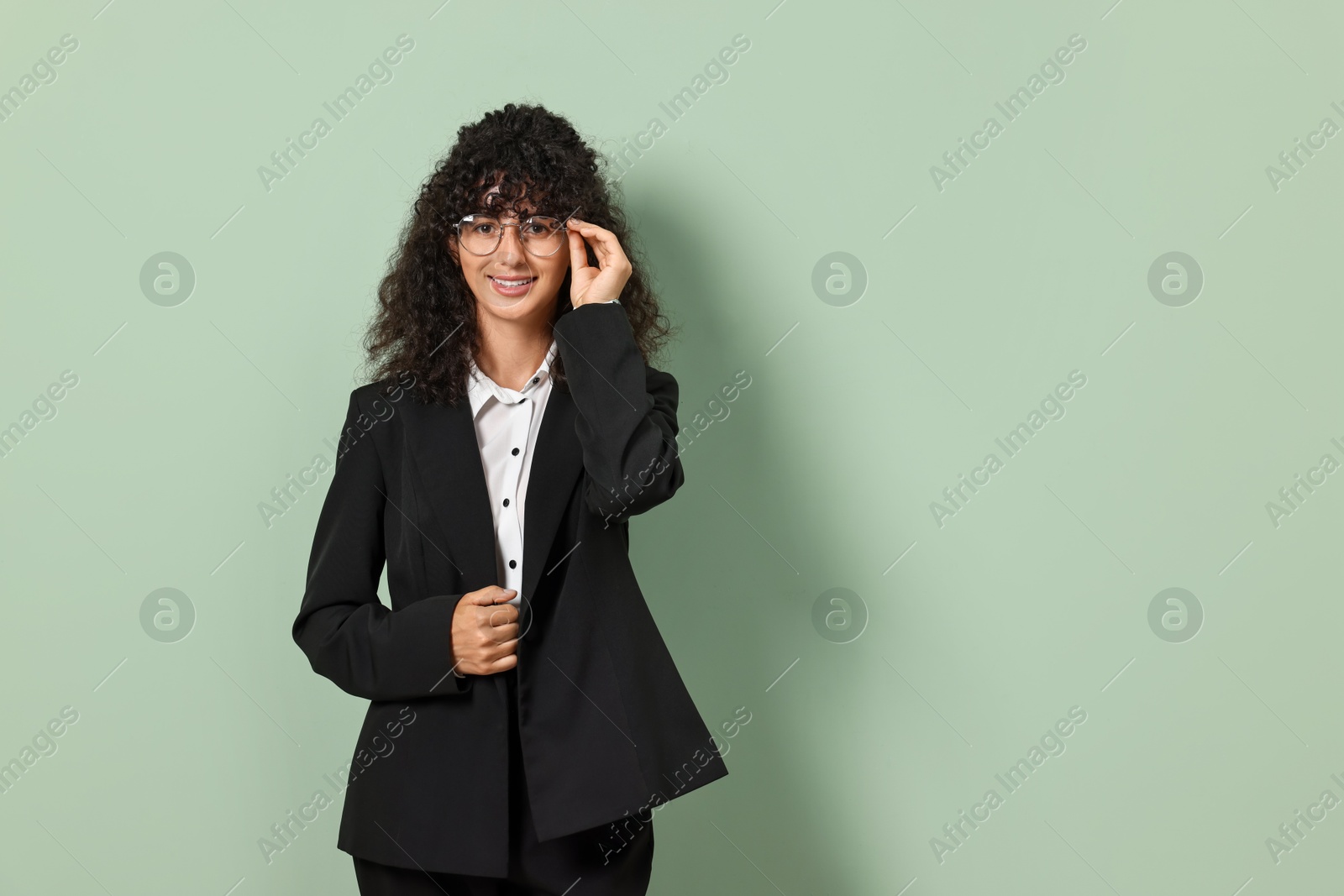 Photo of Beautiful young woman in stylish black suit on light olive background, space for text