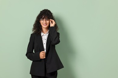 Beautiful young woman in stylish black suit on light olive background, space for text