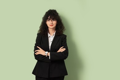 Beautiful young woman in stylish black suit on light olive background, space for text