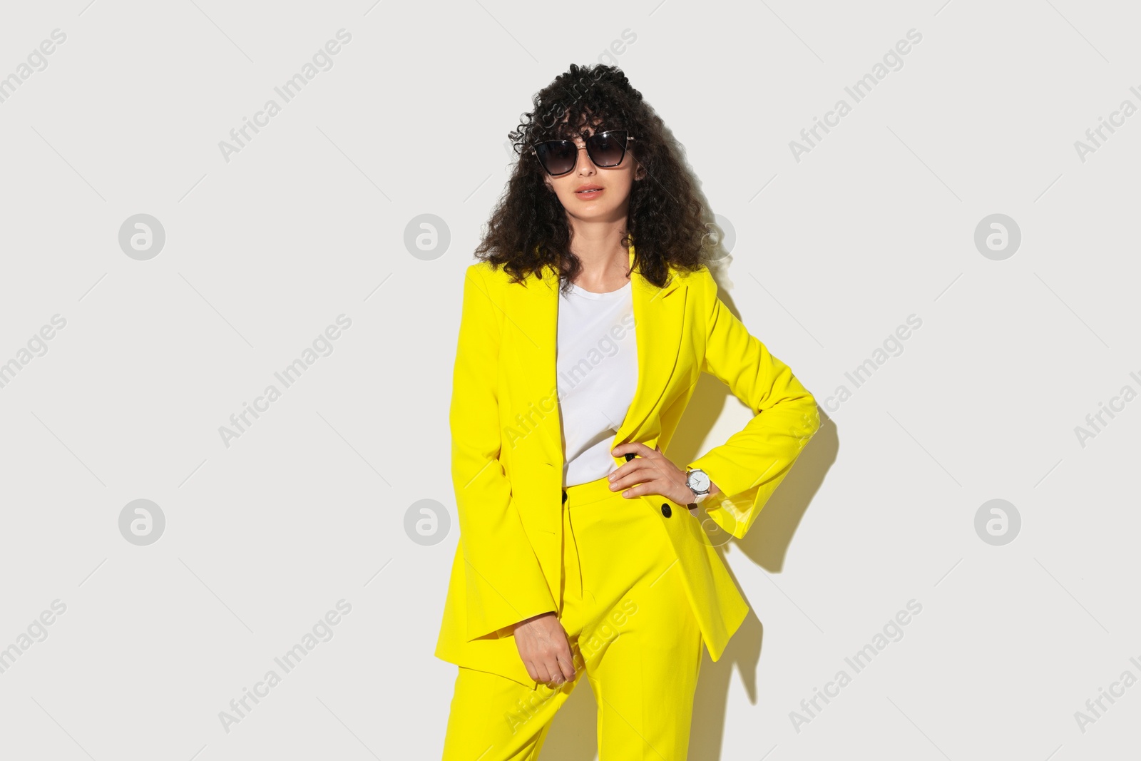 Photo of Beautiful young woman in stylish yellow suit and sunglasses on light background