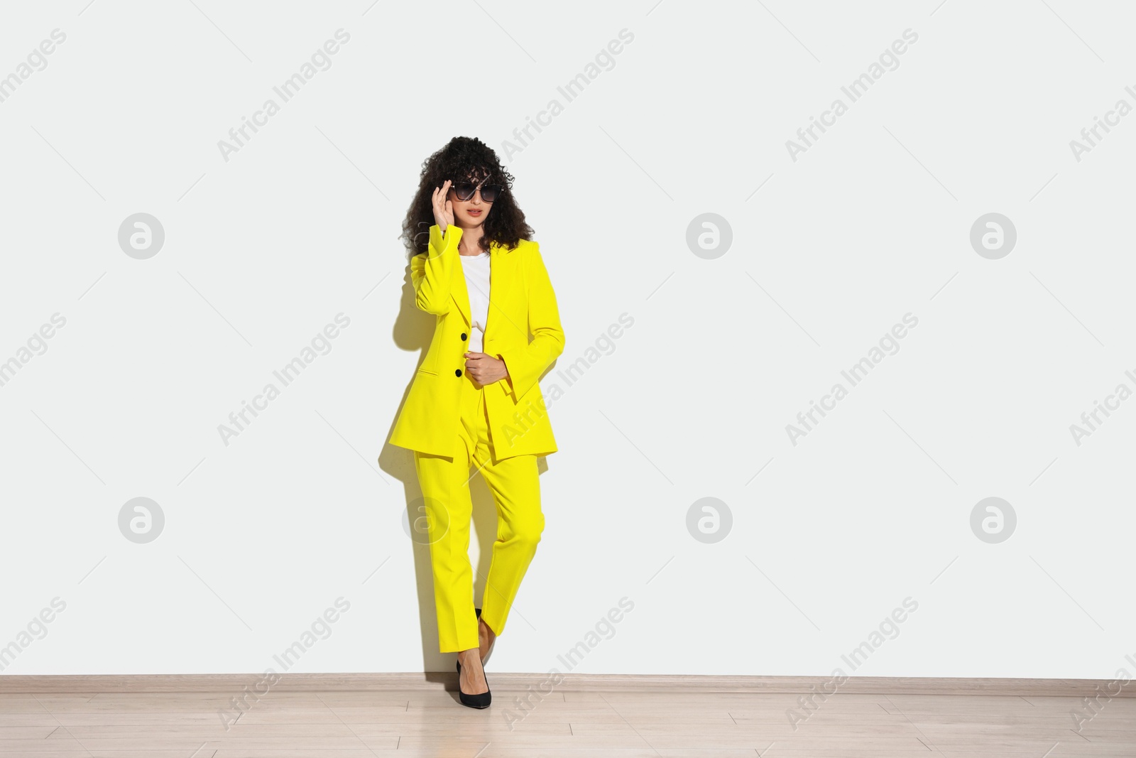 Photo of Beautiful young woman in stylish yellow suit and sunglasses near light wall, space for text