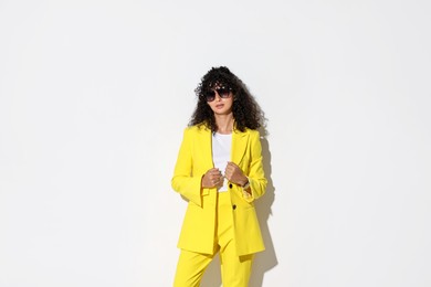 Beautiful young woman in stylish yellow suit and sunglasses on light background