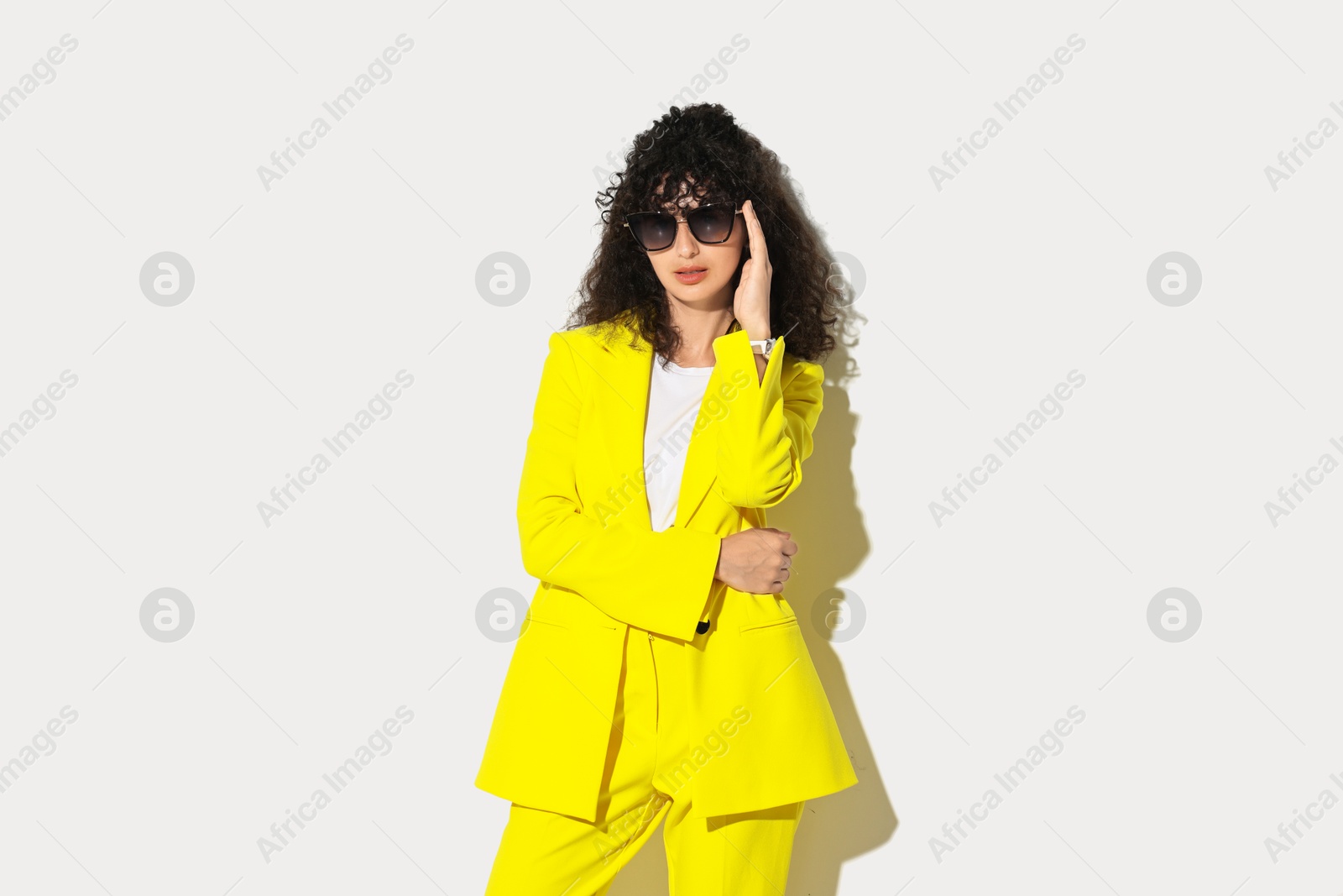 Photo of Beautiful young woman in stylish yellow suit and sunglasses on light background