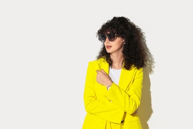 Beautiful young woman in stylish yellow suit and sunglasses on light background, space for text