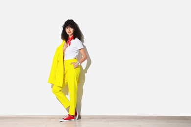 Photo of Beautiful young woman in stylish yellow suit near light wall, space for text