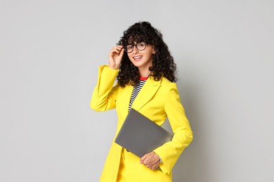 Beautiful young woman in stylish yellow suit with laptop on grey background