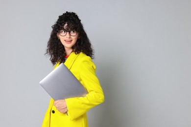 Beautiful young woman in stylish yellow suit with laptop on grey background, space for text