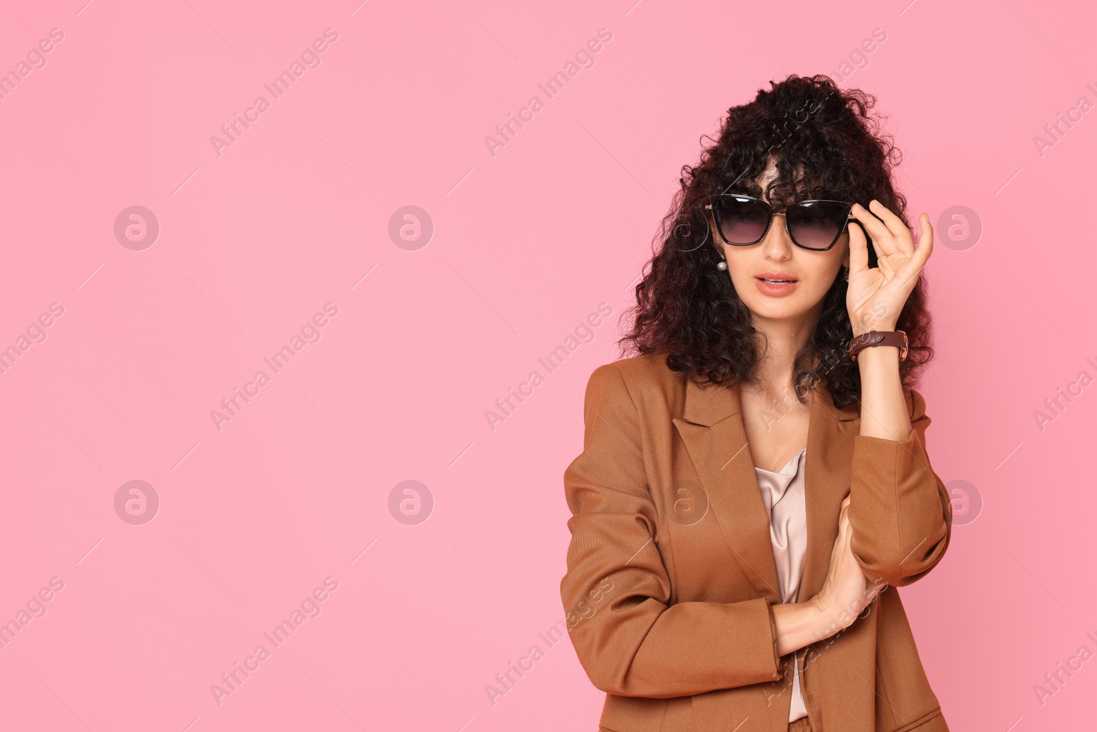 Photo of Beautiful young woman in stylish suit and sunglasses on pink background, space for text