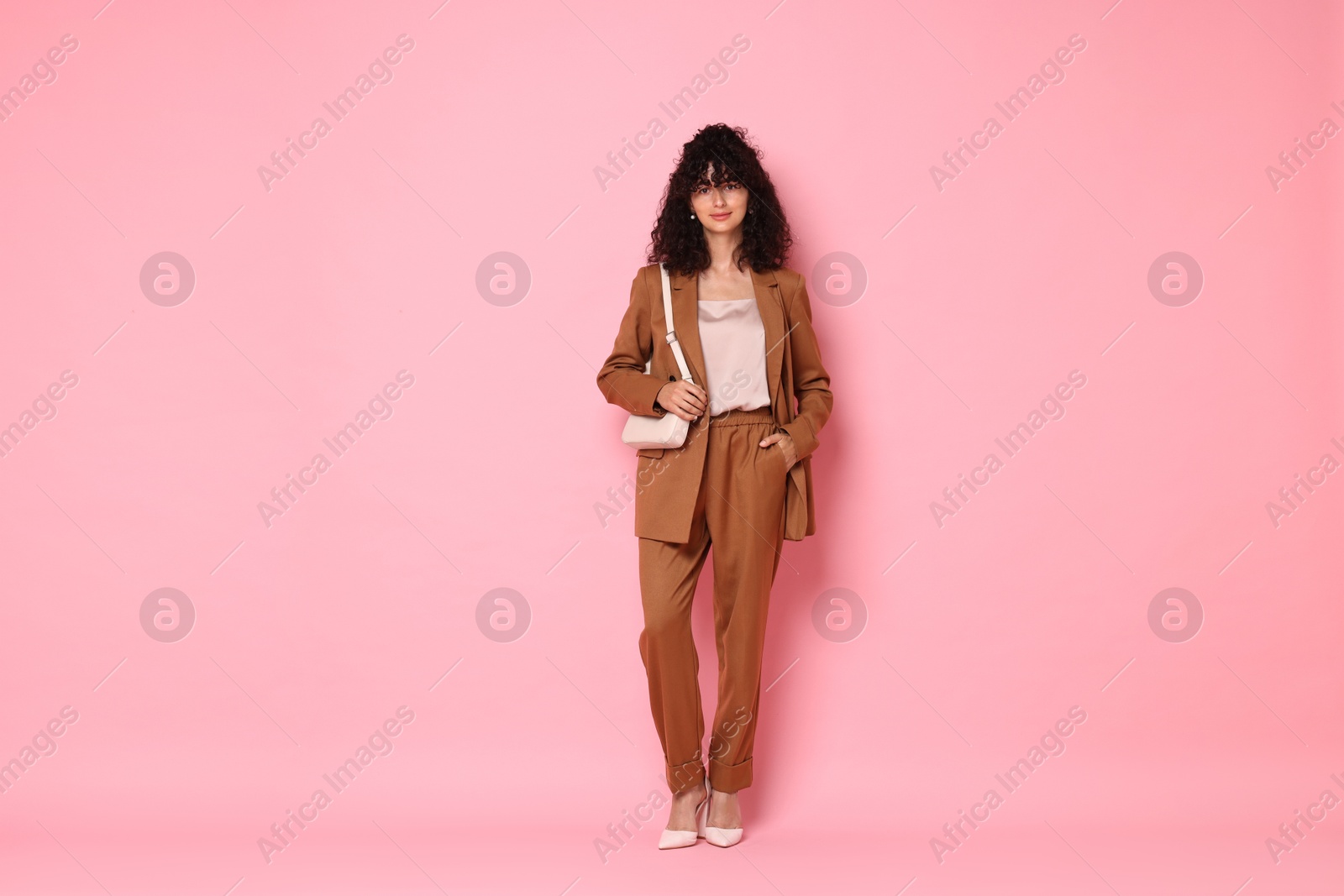 Photo of Beautiful young woman in stylish suit with bag on pink background