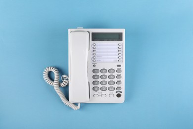 Photo of White telephone with handset on light blue background, top view