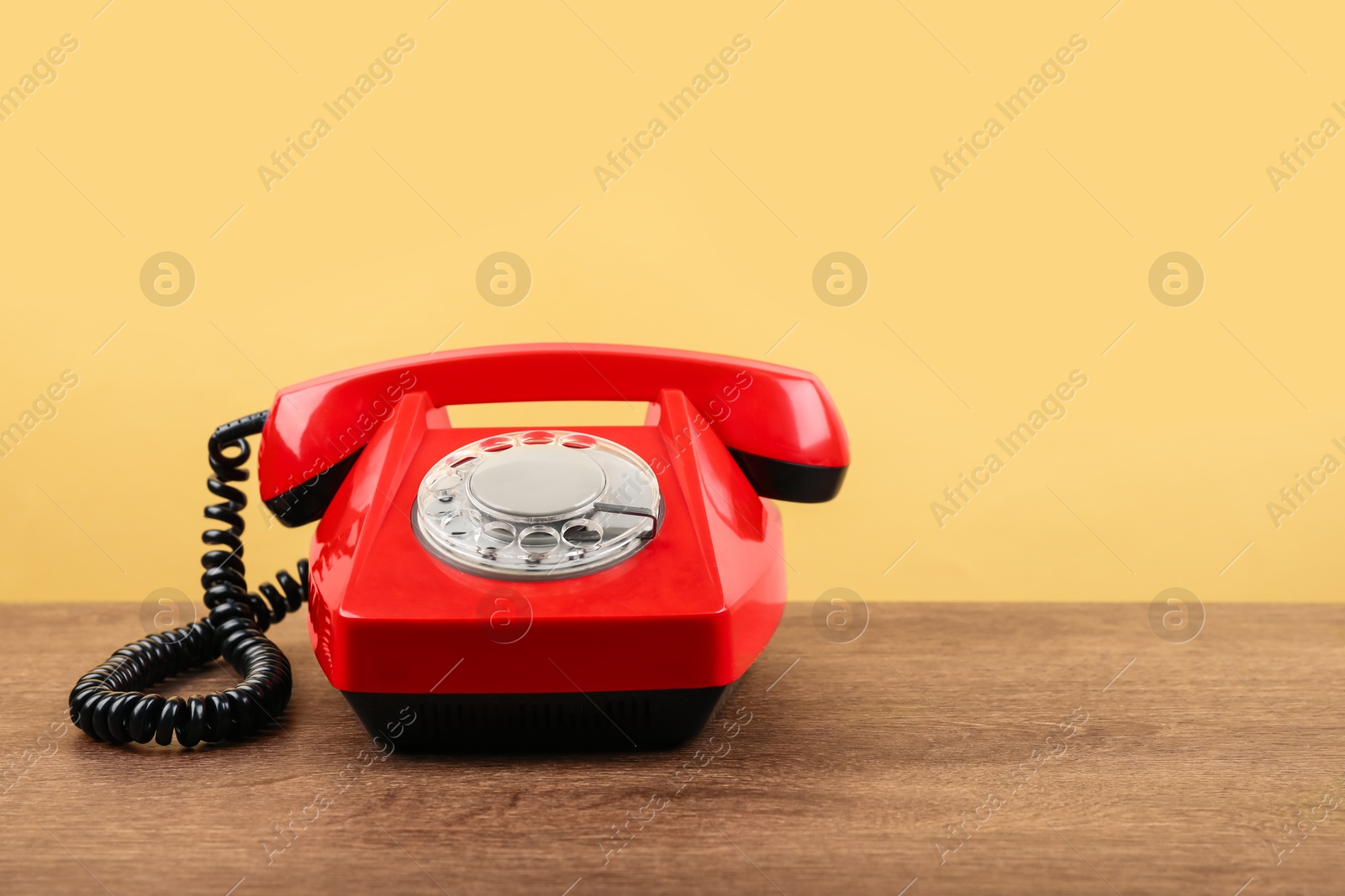 Photo of Red telephone with handset on wooden table against beige background, space for text