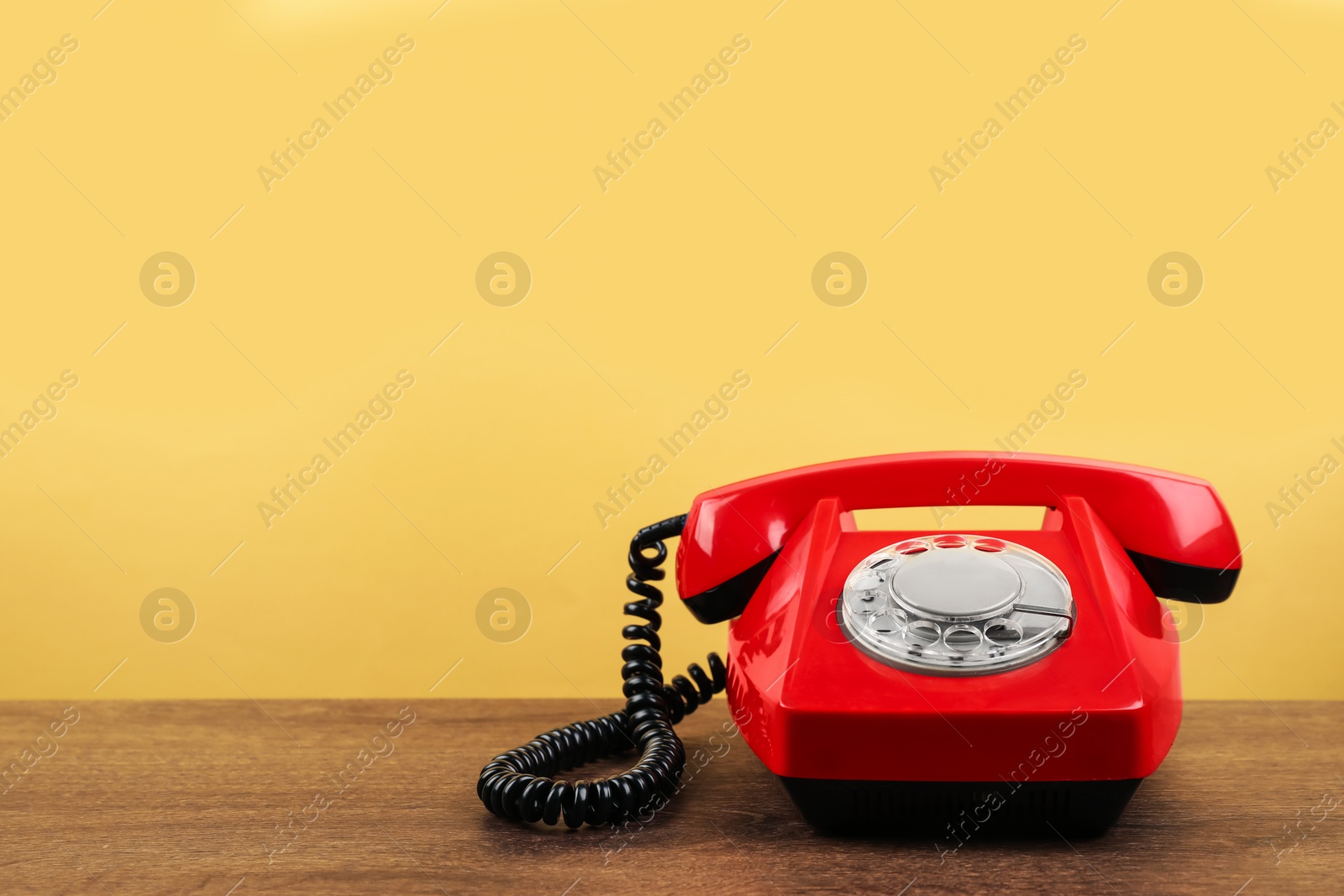 Photo of Red telephone with handset on wooden table against beige background, space for text