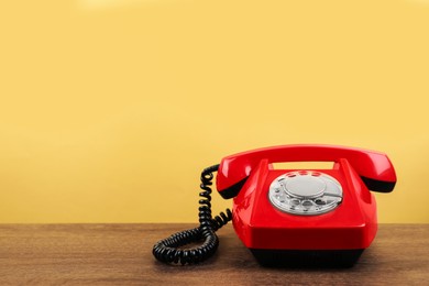 Photo of Red telephone with handset on wooden table against beige background, space for text