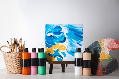 Acrylic paints of different colors, small easel with abstract picture, palette and brushes on wooden table