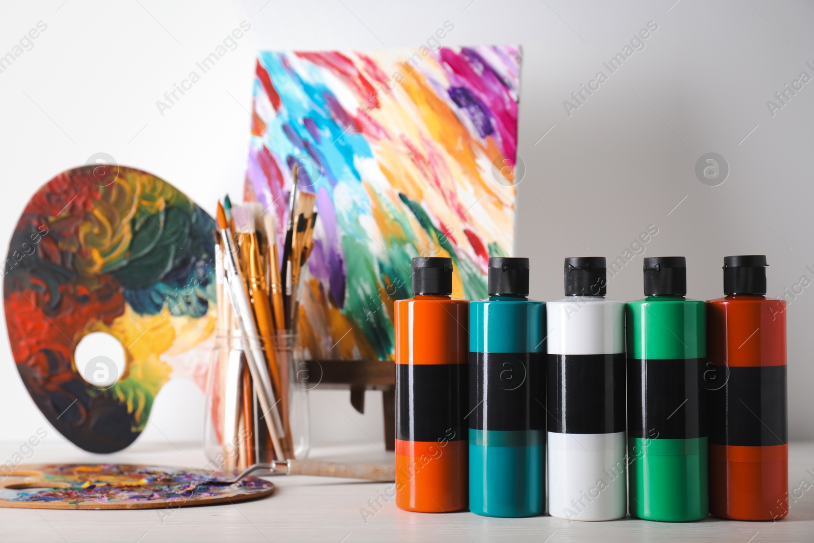 Photo of Acrylic paints of different colors, palettes, knife, small easel and brushes on wooden table