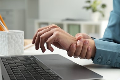 Photo of Carpal tunnel syndrome. Woman suffering from pain in wrist at desk indoors, closeup