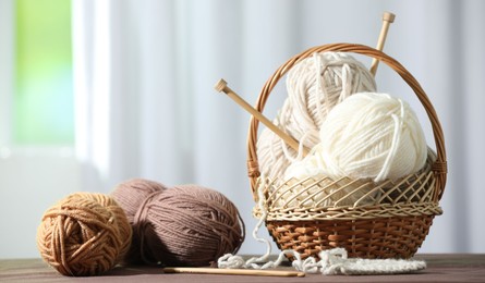 Photo of Skeins of soft yarn and knitting needles on brown fabric indoors