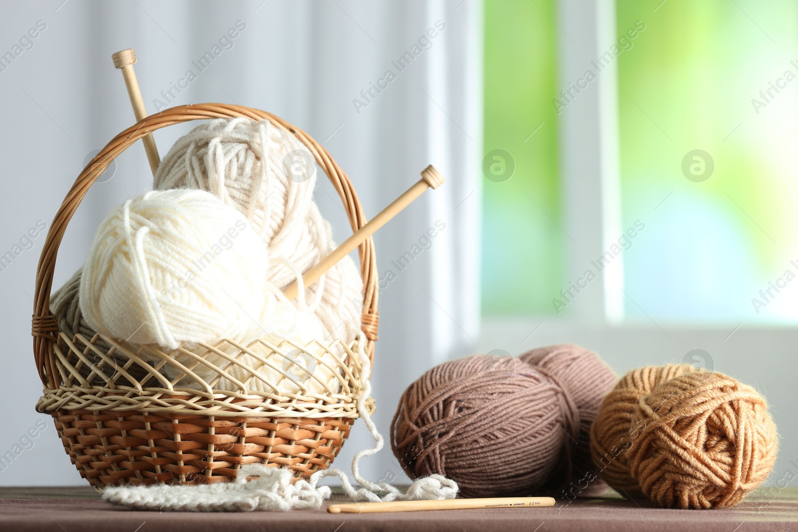 Photo of Skeins of soft yarn and knitting needles on brown fabric indoors