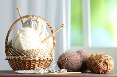 Photo of Skeins of soft yarn and knitting needles on brown fabric indoors