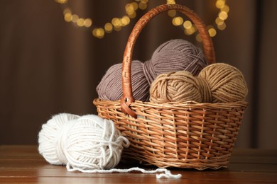 Photo of Knitting material. Wicker basket with skeins of soft yarn on wooden table