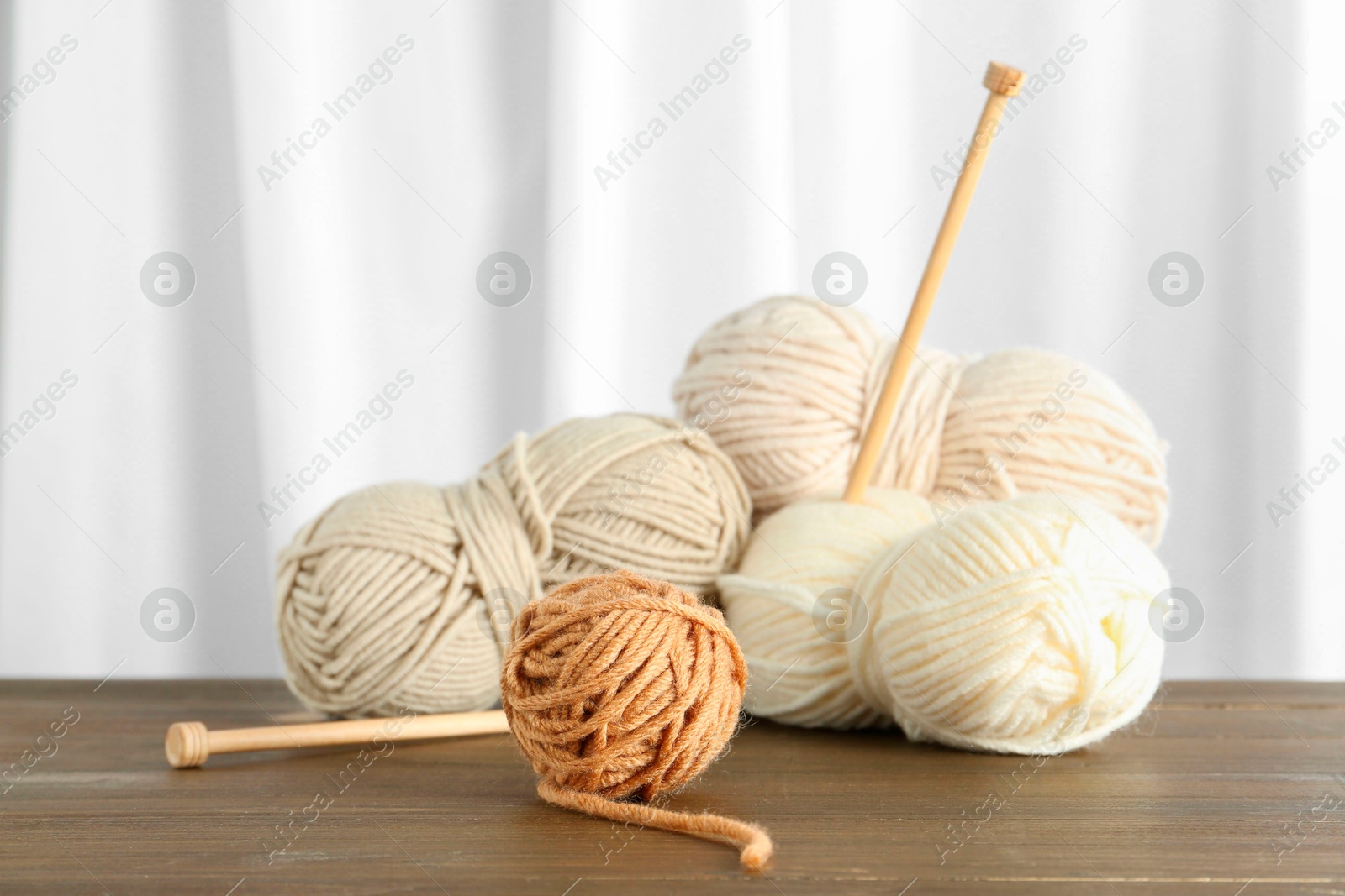 Photo of Skeins of soft yarn and knitting needles on wooden table indoors