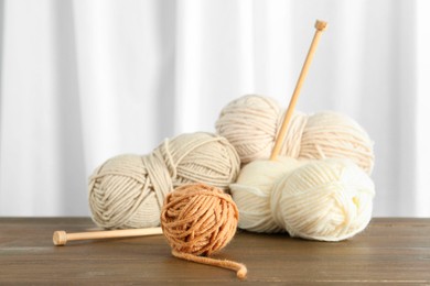 Photo of Skeins of soft yarn and knitting needles on wooden table indoors