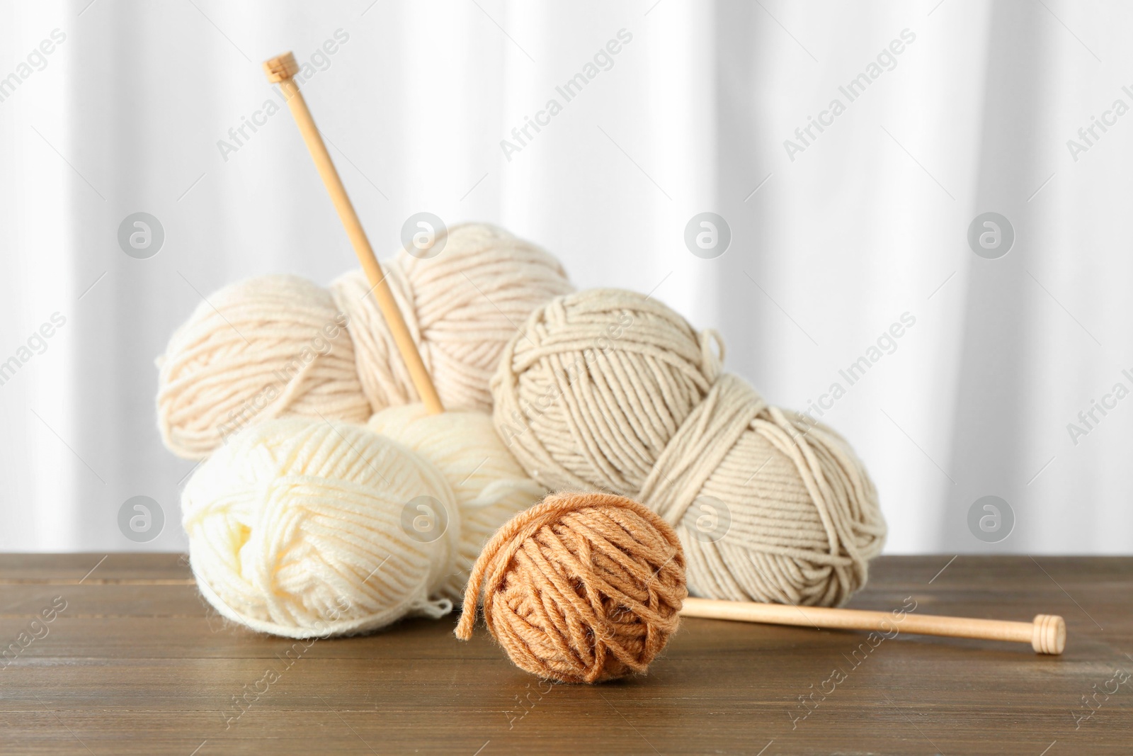 Photo of Skeins of soft yarn and knitting needles on wooden table indoors