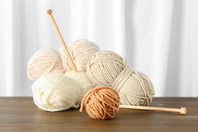 Photo of Skeins of soft yarn and knitting needles on wooden table indoors