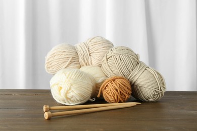 Photo of Skeins of soft yarn and knitting needles on wooden table indoors